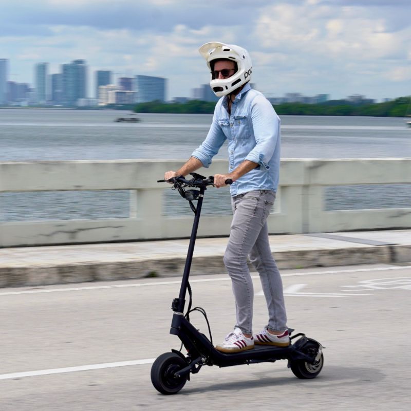 Helmeted rider using a NAMI KLIMA performance electric scooter beside an urban waterfront