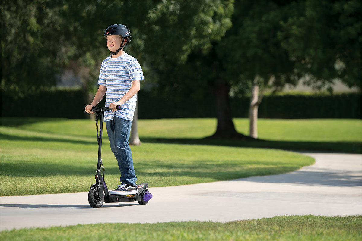 Helmeted young rider using a purple Razor Power Core E100 scooter in a park